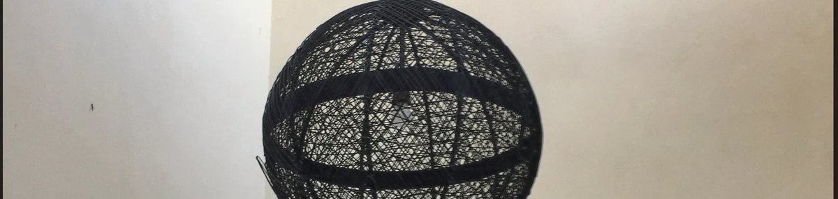 A black woven sphere pendant fixture hanging against a white wall