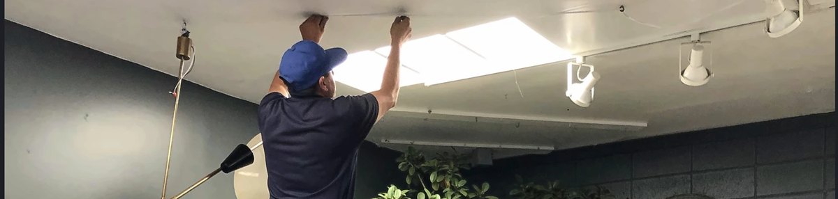 A technician on a ladder repairing a ceiling light fixture