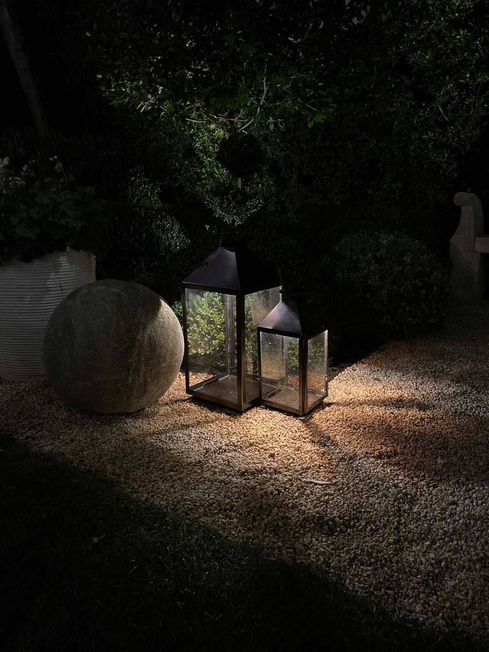 A pair of lantern fixtures glowing on gravel at night